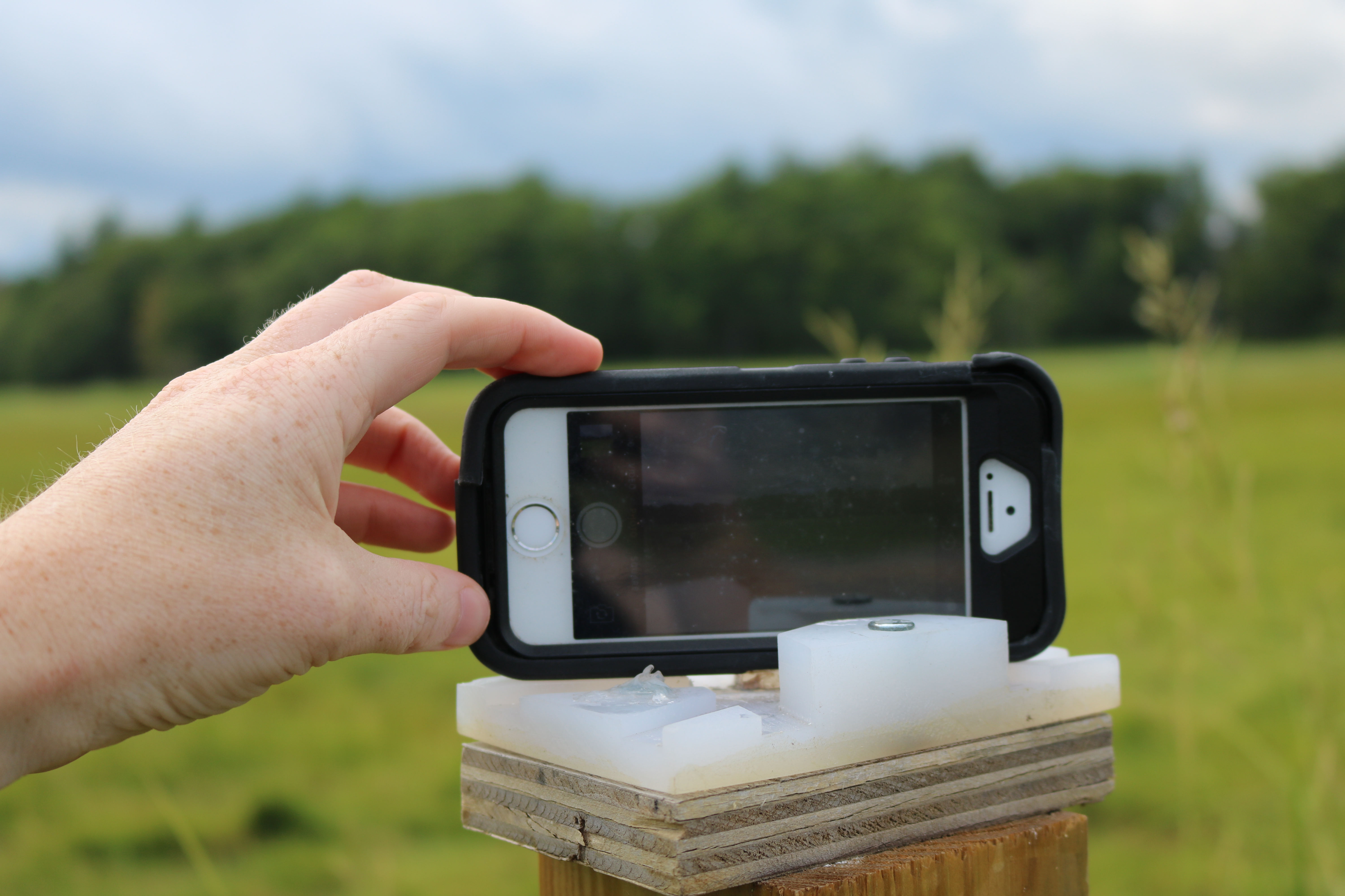 A phone held in Picture Post stand on a post with a hand holding it