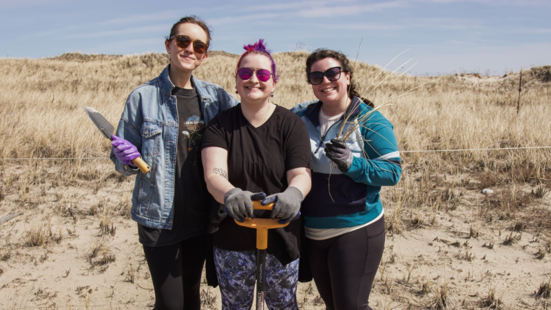 three volunteers with shovel smiling on sand dune