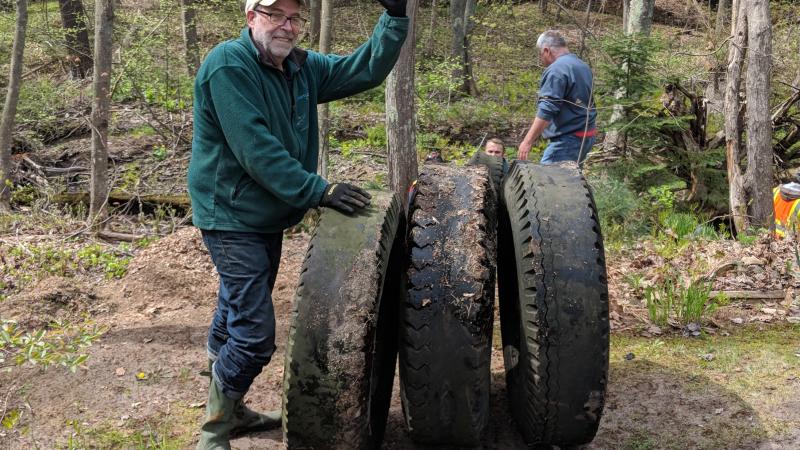 Volunteer cleaning up large tires in a forest