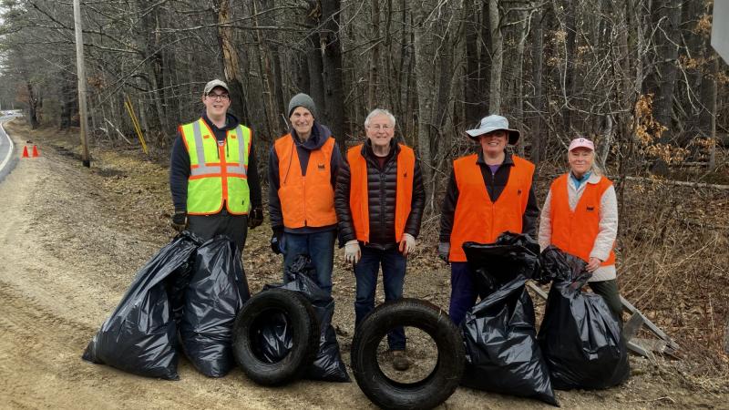 five people standing with bags of trash