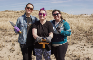 three volunteers with shovel smiling on sand dune