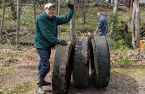 Volunteer cleaning up large tires in a forest